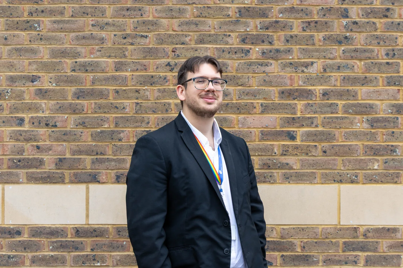 Alex Crean standing against a brick wall with his hands in his pockets, smiling