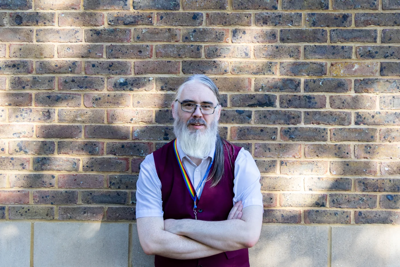 Andrew Lucas standing with his arms folded against a sunlit brick wall